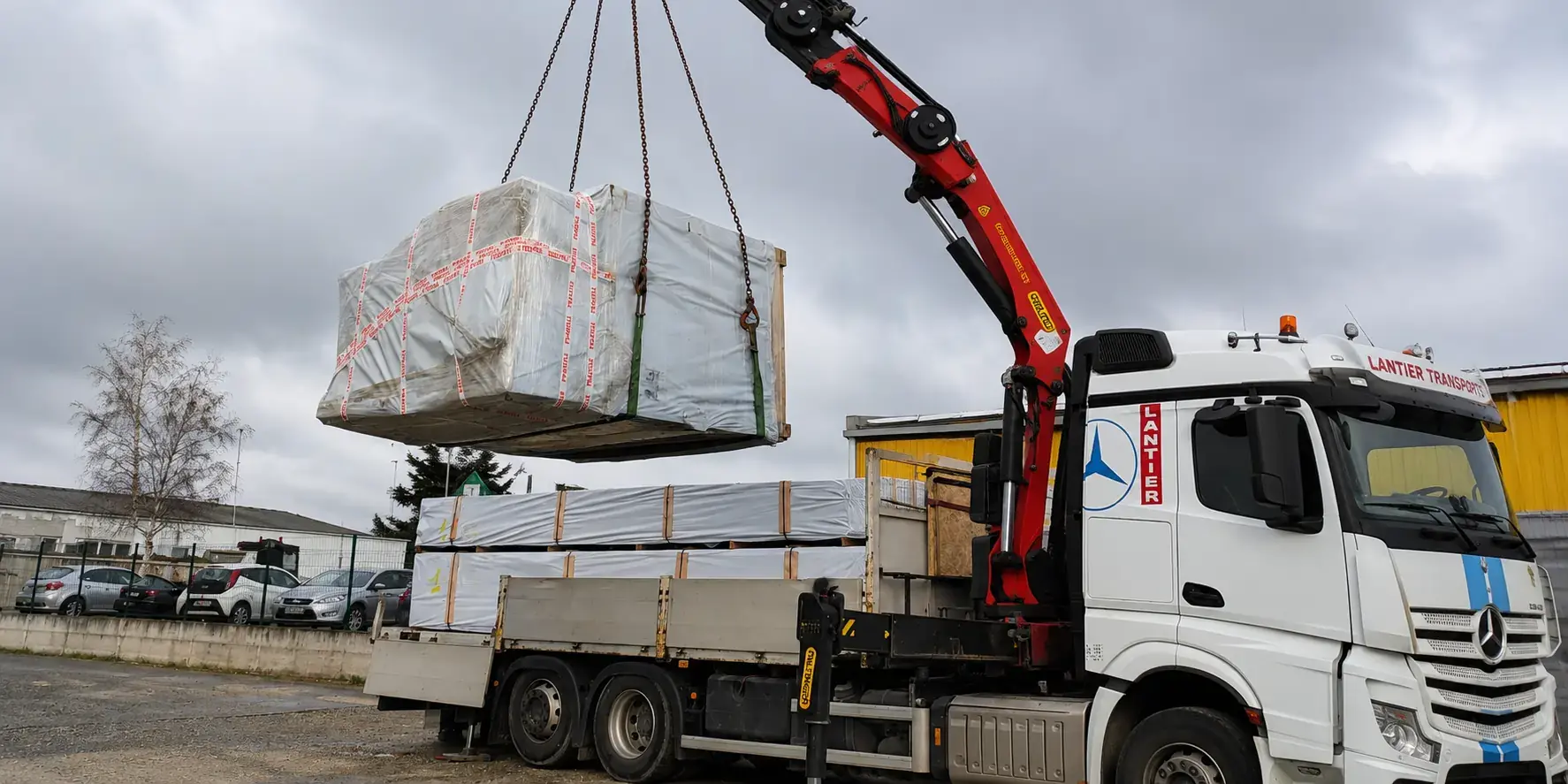 Déchargement d'un kit chalet bois à l'aide d'une grue sur camion pour une livraison à domicile sécurisée.