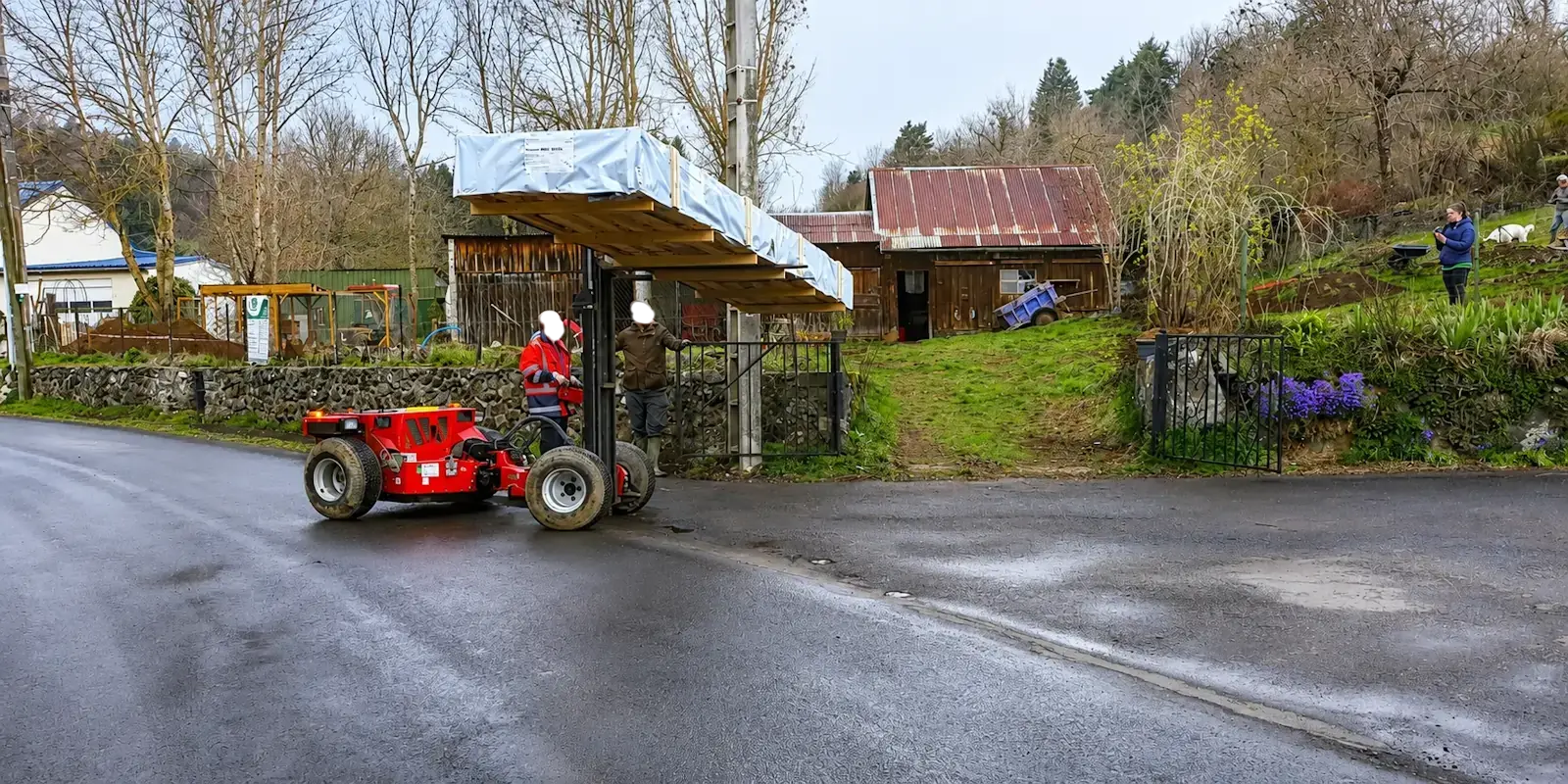Livraison d'un chalet en bois sur une route étroite avec un chariot tout-terrain pour accéder au terrain du client.