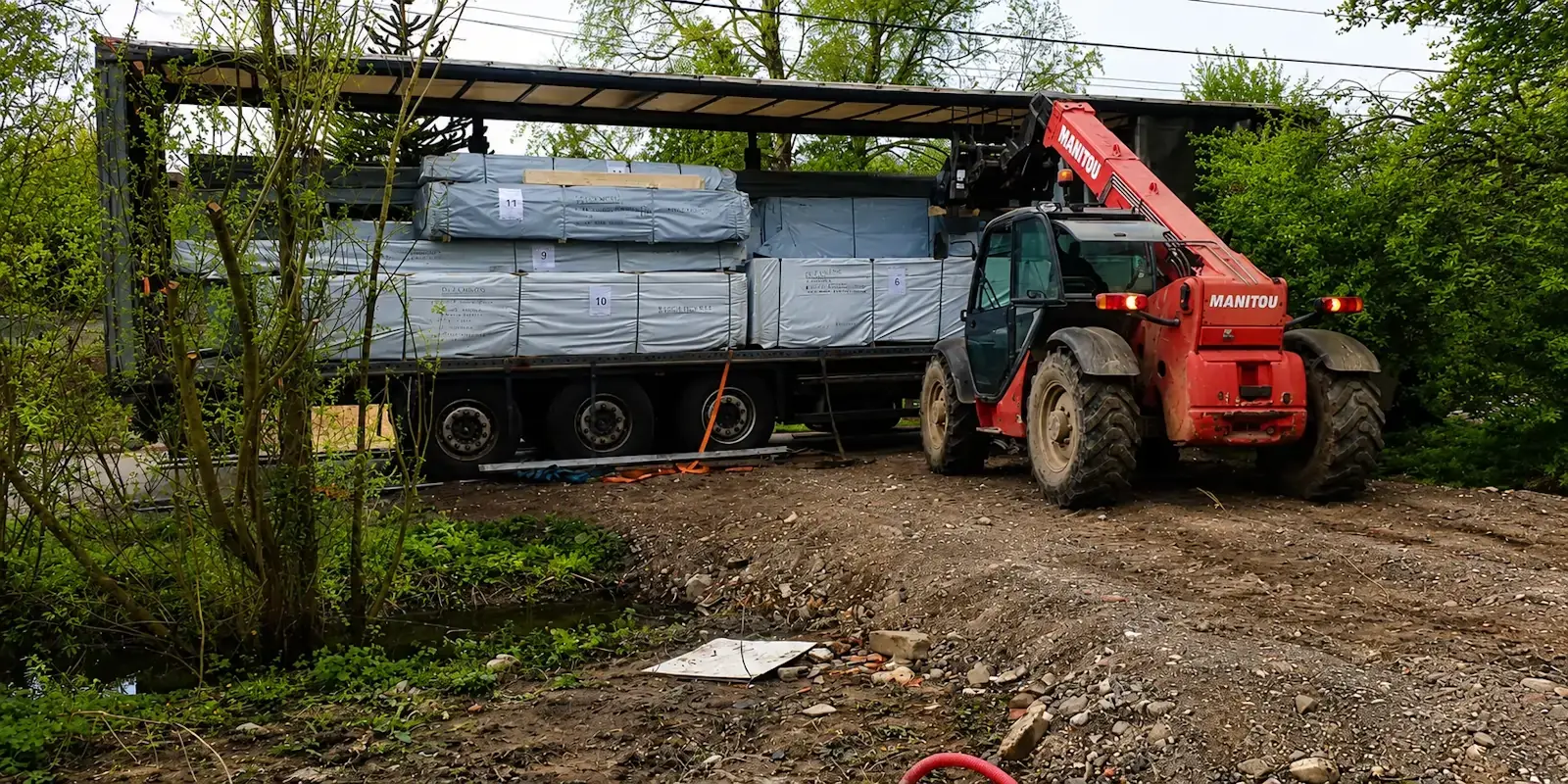Déchargement d'un chalet en bois en kit avec un chariot télescopique Manitou lors d'une livraison à domicile réalisée par STMB Construction.