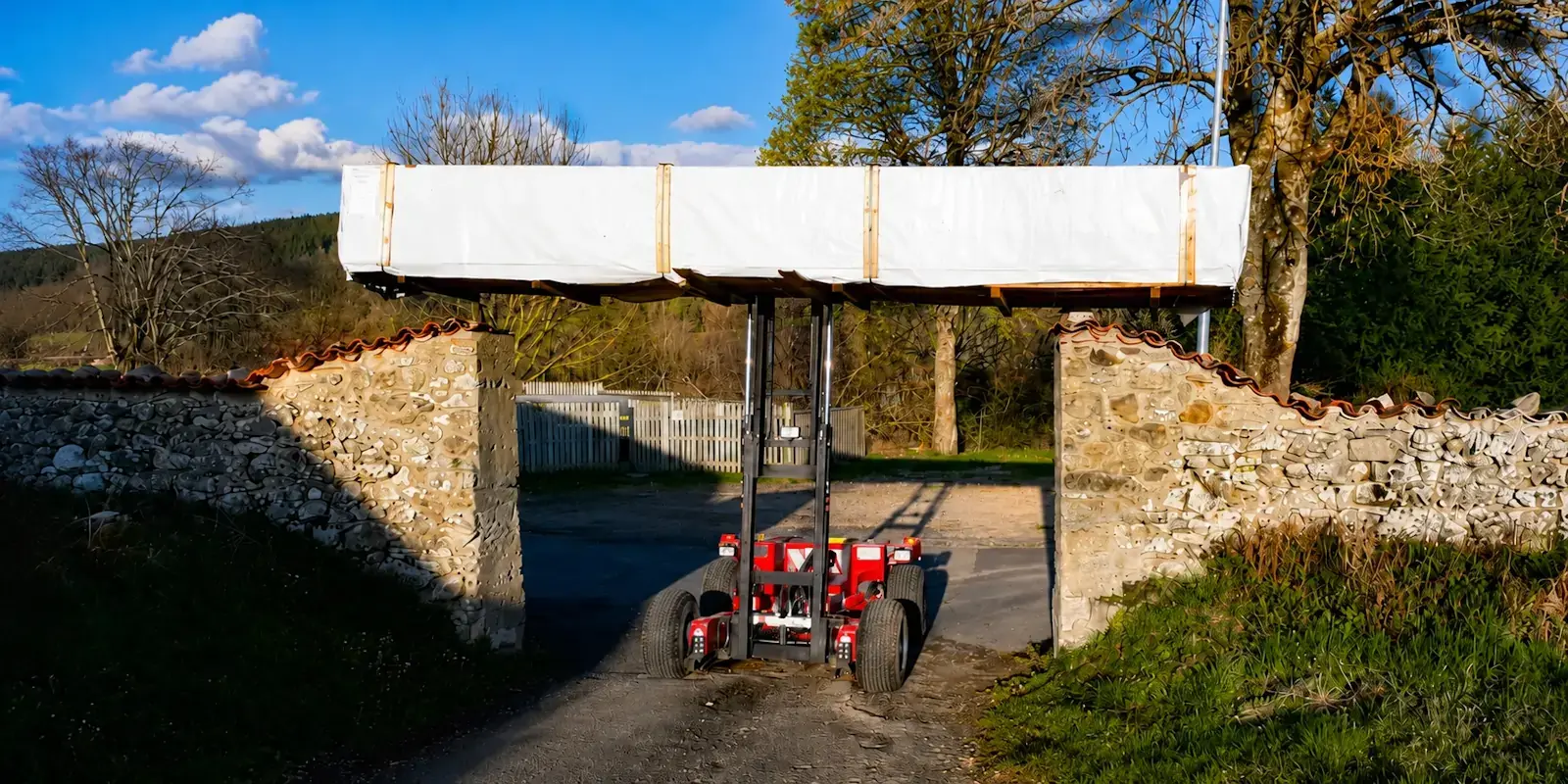 Livraison d'un chalet en bois à travers un portail étroit avec un chariot tout-terrain pour accéder au terrain du client.